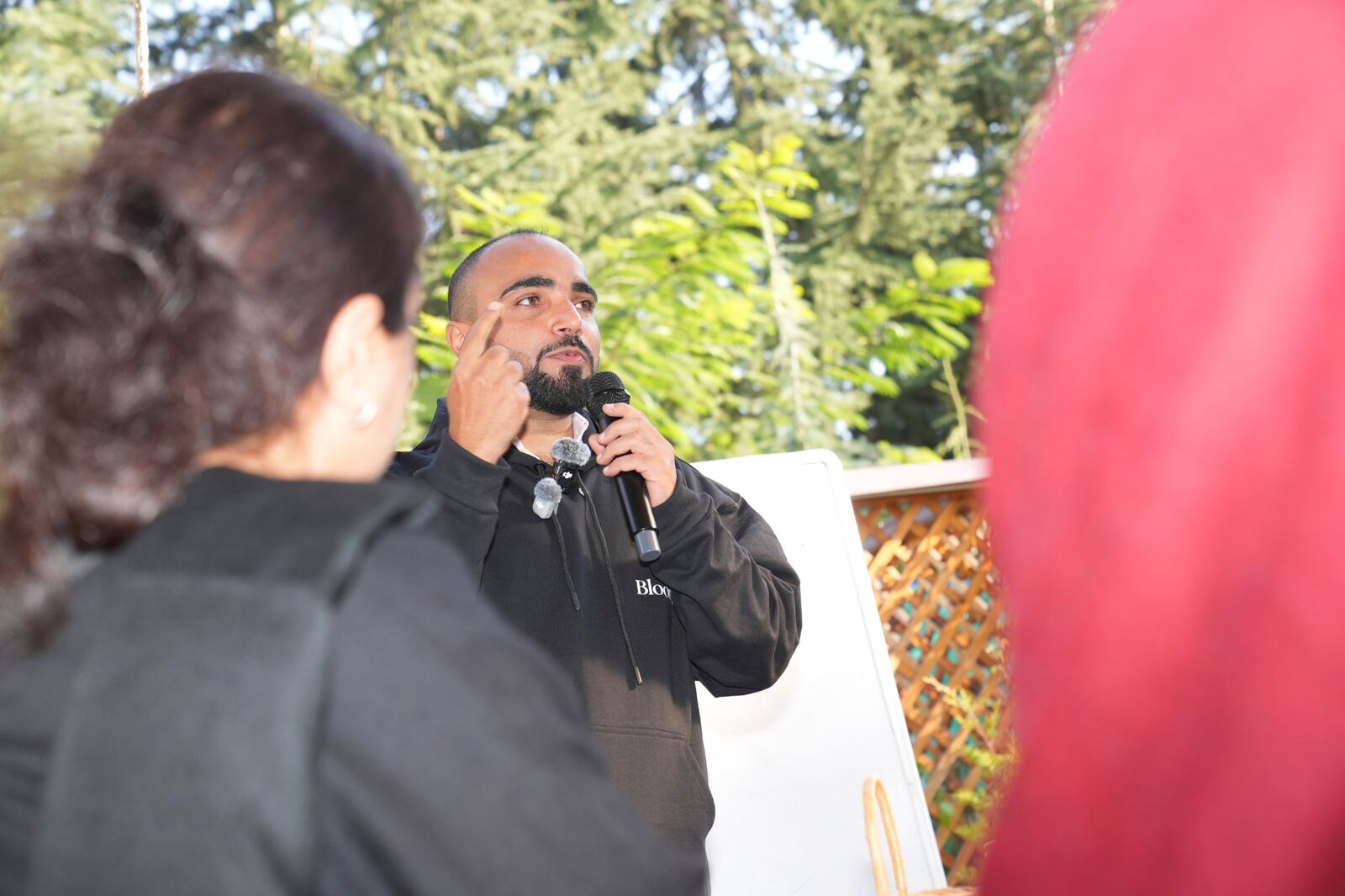Farhat Umar speaking with a microphone at an outdoor Compass session